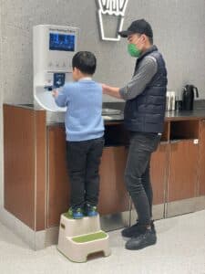 Child using a Smixin automatic handwashing station with an adult